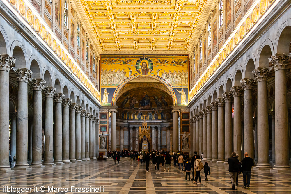 Navata centrale della Basilica di San Paolo fuori le Mura con colonnati monumentali, soffitto dorato e fedeli in cammino verso l’abside
