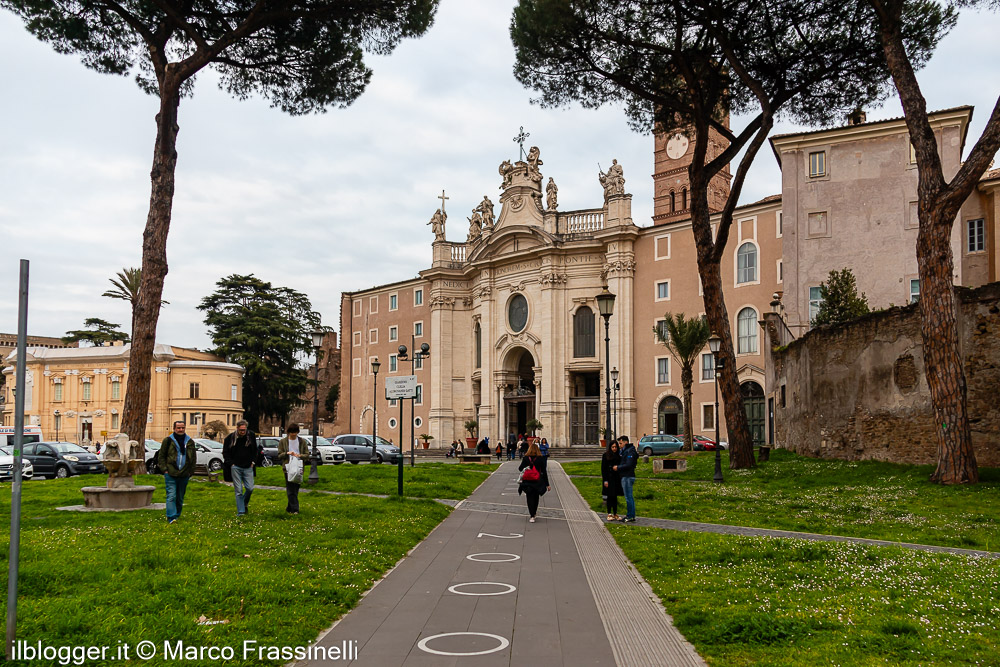 Percorso pedonale che conduce alla Basilica di Santa Croce in Gerusalemme, con area verde alberata e facciata monumentale sullo sfondo